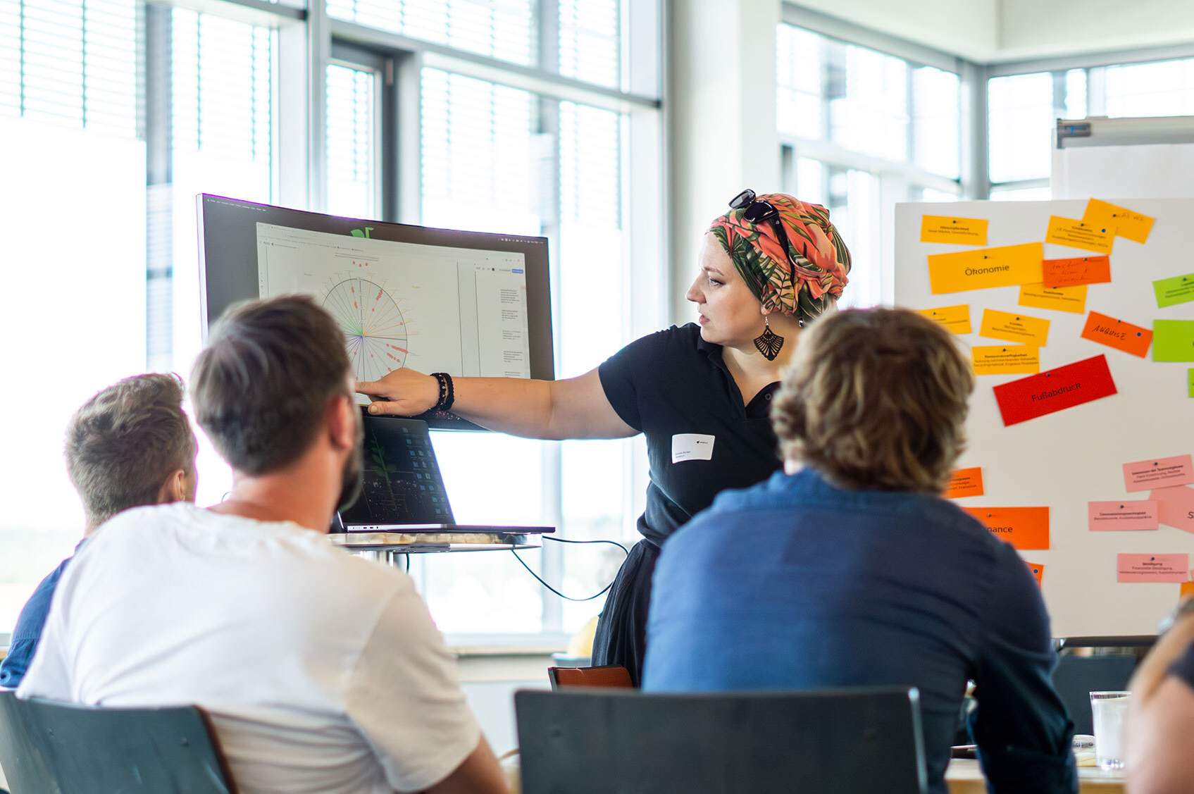 KI generiert: Das Bild zeigt eine Gruppe von Menschen in einem modernen Büro, die konzentriert an Laptops arbeiten und sich dabei unterhalten.