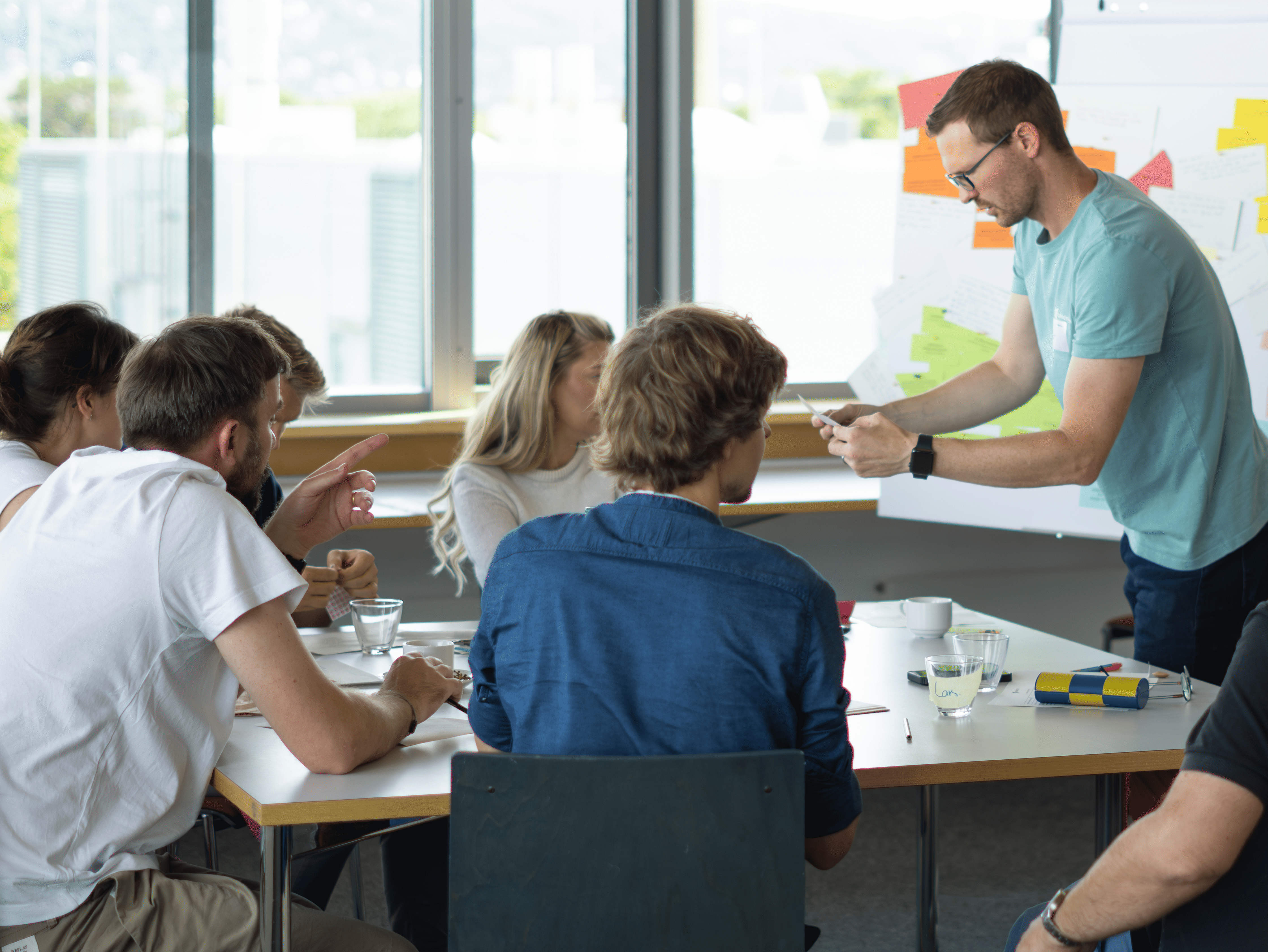 KI generiert: Das Bild zeigt eine Gruppe von Menschen in einem Seminarraum, die konzentriert an Laptops arbeiten und Notizen machen, während eine Person eine Präsentation hält.