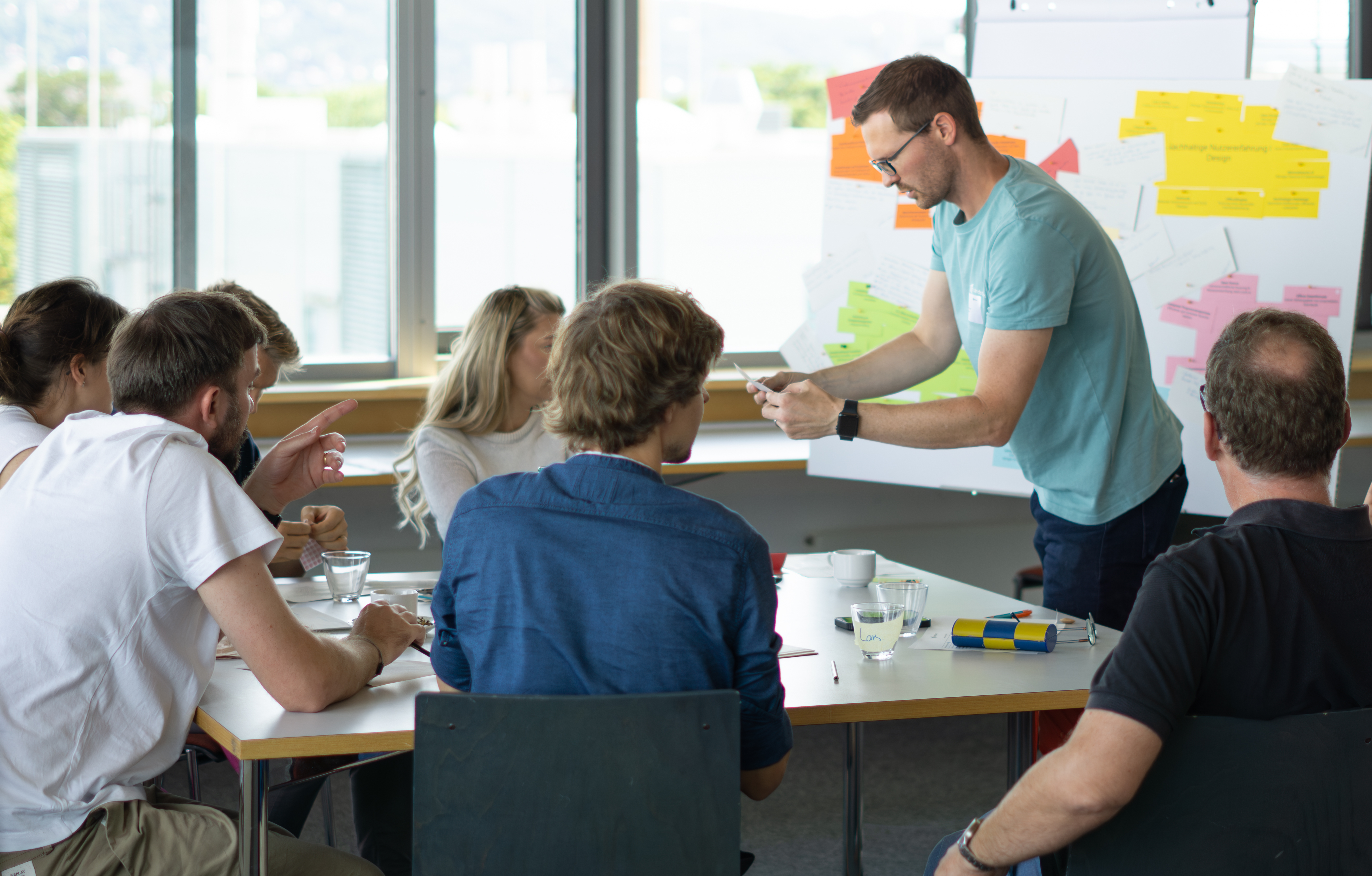 KI generiert: Das Bild zeigt eine Gruppe von Menschen in einem Raum, die an einem Workshop oder Seminar teilnehmen, bei dem eine Person etwas an einem Flipchart erklärt.